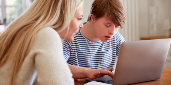 Downs Syndrome Man Sitting With Home Tutor Using Laptop For Lesson At Home Downs Syndrome Man Sitting With Home Tutor Using Laptop For Lesson At Home